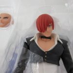 本体上半身のクローズアップ。黒いジャケットと赤い髪、交換用表情パーツが見える。