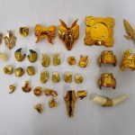 金色の聖衣パーツ、交換用の手、小物を並べたところ。