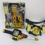 金色のライオンをあしらったベルトと、箱入りのリングホルダー、黒と金の剣型の品を並べたところ。