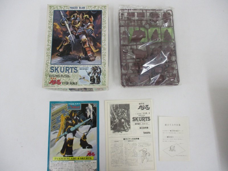 外箱と袋に入った茶色のランナー、カード、組立説明書を並べて撮影。説明書に SKURTS の印字があります。