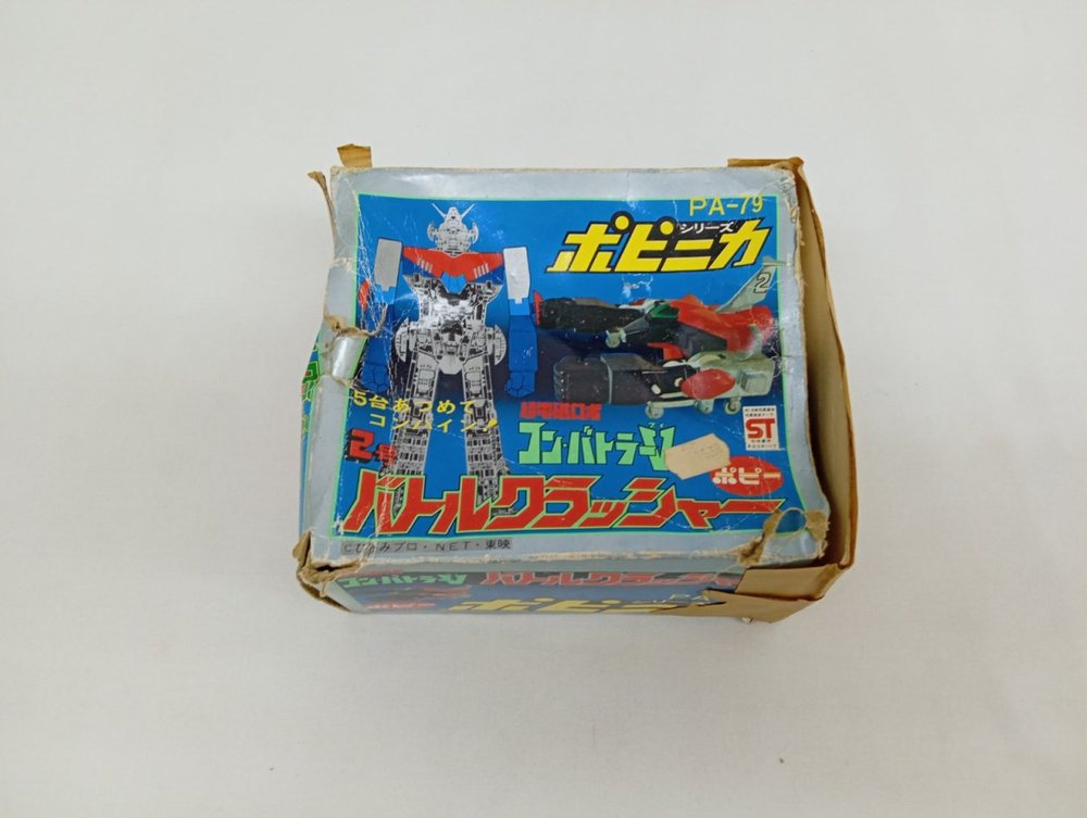 箱のふたの正面。『PA-79』『ポピニカ シリーズ』『バトルクラッシャー』の印刷と機体の絵。角に破れ
