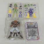 透明トレイが2段。上段に緑の髪のフィギュアと細かいパーツ、下段に褐色の大型フィギュアと注意書きの紙があります。