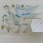 透明トレイに入ったメッキのパーツと大型の翼、白い台座が写っています。