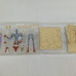透明トレイに入った銀色の素体と、柱のような造形のパーツ、台座状のパーツ。