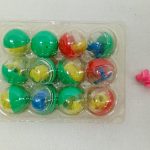 透明ケースに入った色とりどりのカプセルと、右にピンクの小さな部品。