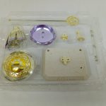 透明トレイのアップ。紫の円盤、金色の円盤、白い台座の部品