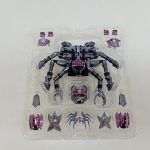 透明トレイに収まった蟹の形の黒い飾りと、周りに並ぶ聖衣の部品