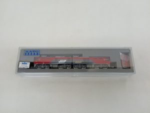 透明ケースに入った車両を斜め上から撮った写真。赤とグレーの電気機関車が収まっています。