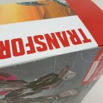 外箱の上面のアップ。赤い帯の上に「TRANSFORMERS」の白抜き文字。