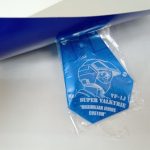 袋に入った青いタグのアップ。『VF-1J SUPER VALKYRIE』『MAXIMILIAN JENIUS CUSTOM』の文字