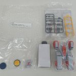 袋に入った部品一式。ランナー、灰色と赤の艦体パーツ、円形の台座パーツ、白い箱。