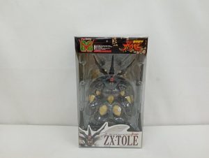 透明のプラスチック箱の正面。中に濃い茶色のフィギュアが収まり、下に「ZX・TOLE」の表示があります。