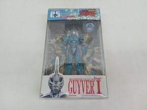 透明なプラスチック箱の正面。中に青緑色の本体、下の台紙に「BIO FIGHTER COLLECTION GUYVER I」の印字。