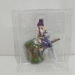 ブリスターに入ったフィギュアを正面から。紫の忍装束の女性が切り株に座っている