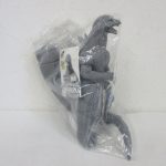 袋に入った本体とタグ。二足で立つ灰色の怪獣です。