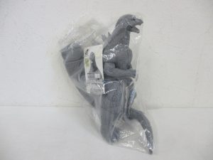 袋に入った本体とタグ。二足で立つ灰色の怪獣です。
