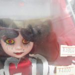 ケース越しに撮影した人形の顔。黒い髪と黄色い目、赤い服の造形です。