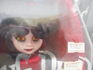 ケース越しに撮影した人形の顔。黒い髪と黄色い目、赤い服の造形です。
