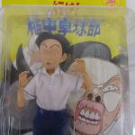 ブリスター越しに撮影した人形の上半身。細い眉と中分けの髪、白い半袖シャツです。