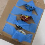 箱の中でテープに留められたベイブレード4個。
