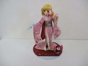 巴マミ 舞妓Ver.の全身。ピンクの振袖を着て、台座にべべが立っています。