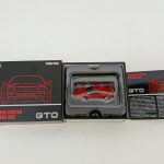 外箱と、トレーに収まった赤いミニカー、解説カードを並べたところ