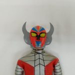 ヘルメットのアップ。赤い顔に黄色い目、左右の銀色の角