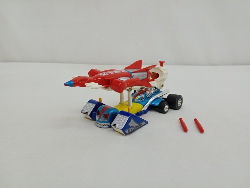 本体を斜め前から写した様子。青いレーシングカーの上に赤い機体が載り、手前に赤いミサイル2本が置かれています。