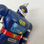 上半身を斜めから。腕の「28」の数字と赤いベルトの「T」マークが写っています。