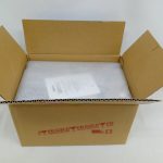 開いた輸送用の段ボール箱の中。白い紙と緩衝材が入っており、箱の側面に「FRAGILE」の赤い印字があります。
