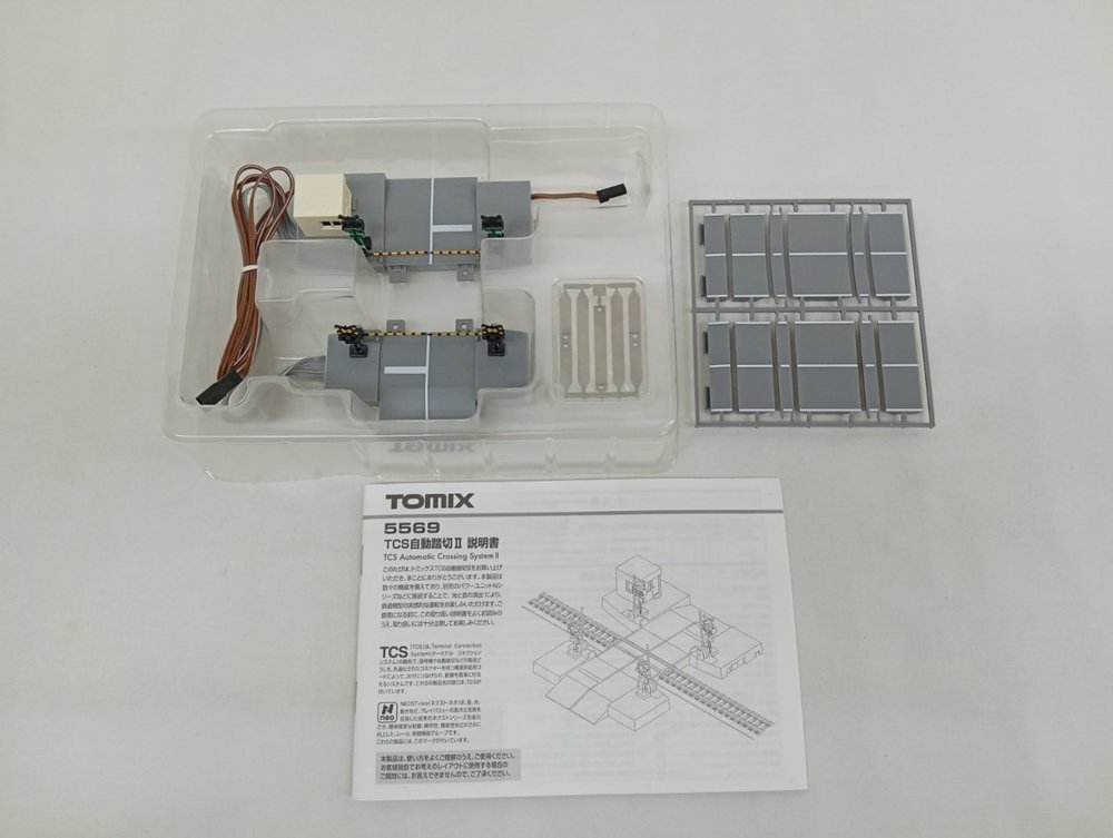 透明ケースに入った踏切のユニット2組と、灰色の部品の枠、TOMIXの説明書を並べた写真。