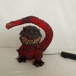 発光させたゴジラのフィギュアを正面から写した写真。胸が赤く光り、電源ユニットにつながっている