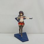 青い台座に立つ黒髪の少女のフィギュアを正面から。赤い眼帯風の飾りとマント