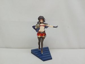 青い台座に立つ黒髪の少女のフィギュアを正面から。赤い眼帯風の飾りとマント